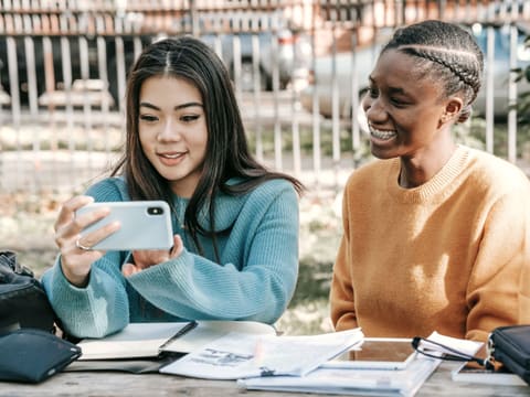 Two friends going through questions together on a phone, notes on the table