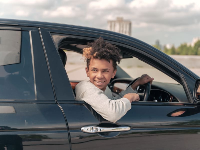 A teenager smiling from the driver's seat of a parked car